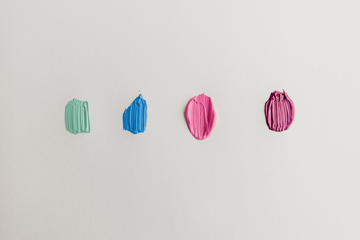 Four paint swatches in green, blue, pink and magenta on a white wall